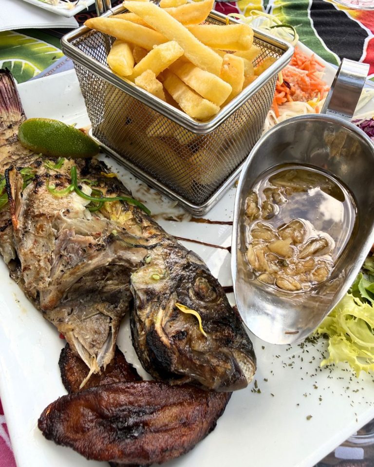 Assiette de poisson grillé avec frites, bananes plantains et sauce au restaurant Chez Lèlette à Deshaies en Guadeloupe, face à la mer.