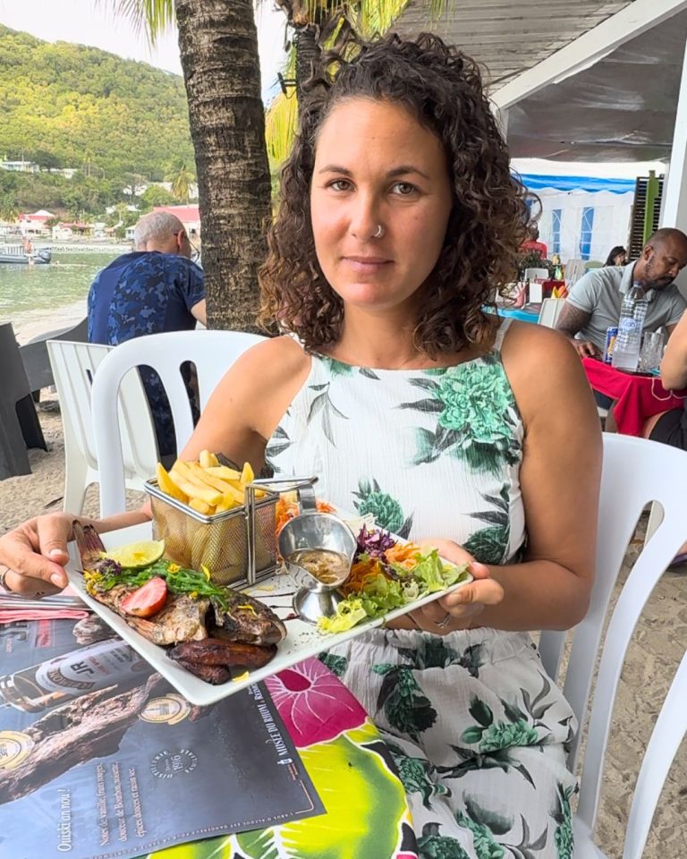 Ambre TAC au restaurant Chez Lèlette à Deshaies en Guadeloupe avec une assiette de poisson grillé, frites et salade dans un restaurant local en bord de mer.