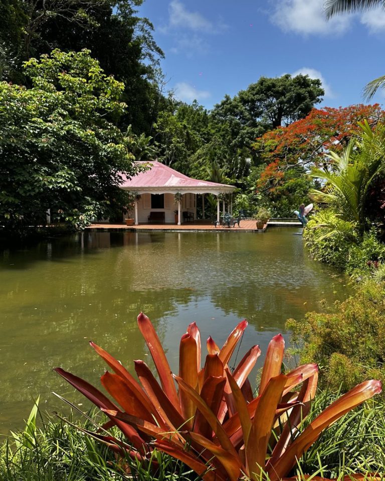 Étang au Jardin botanique de Valombreuse à Petit-Bourg en Guadeloupe avec maison créole et végétation tropicale luxuriante.