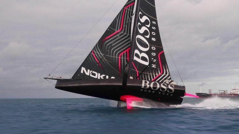 Voilier IMOCA Hugo Boss à foils en pleine navigation lors de la Route du Rhum 2026 – Destination Guadeloupe, bateau noir filant sur l’océan Atlantique.