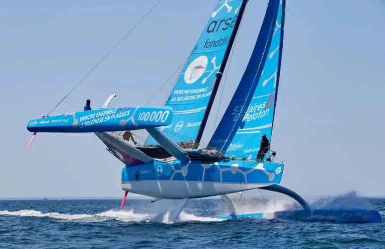 Trimaran Ocean Fifty bleu en pleine vitesse lors de la Route du Rhum 2026 – Destination Guadeloupe, bateau de course survolant les vagues de l’océan Atlantique.