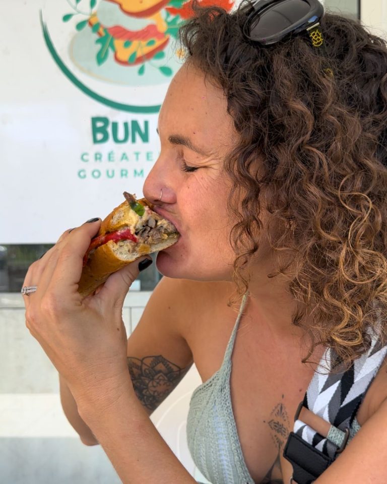 Ambre TAC dégustant un sandwich gourmand du snack Bun Me au Gosier en Guadeloupe avec viande marinée, légumes grillés et pain croustillant préparé maison.