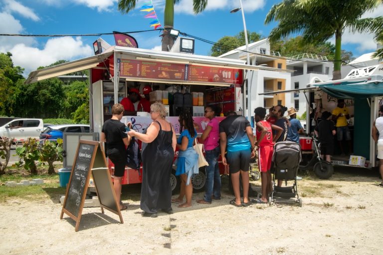 Visiteurs faisant la queue devant un food truck lors de La Foire des Roulottes à Pointe-à-Pitre en Guadeloupe avec restauration rapide, boissons et ambiance conviviale.