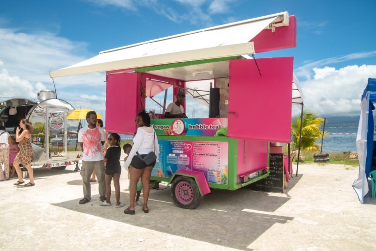 Food truck coloré proposant bubble tea, boissons et restauration lors de La Foire des Roulottes à Pointe-à-Pitre en Guadeloupe avec visiteurs face à la mer.